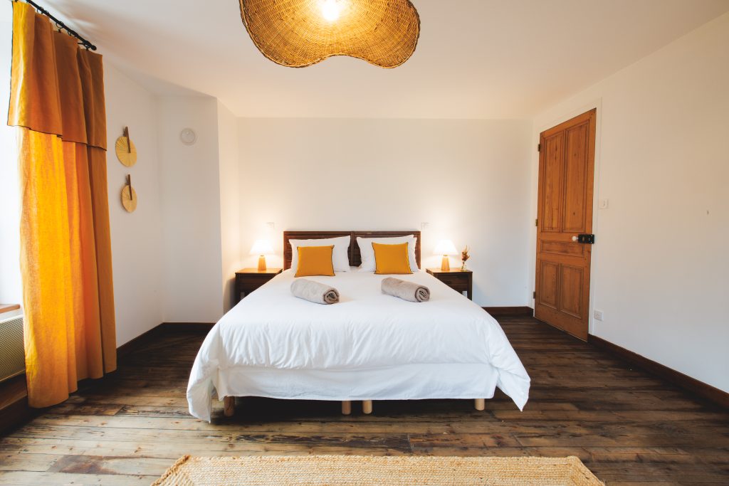 Chambre parentale lumineuse et moderne avec grand lit double, décor chaleureux en bois, éclairage doux et ambiance cosy idéale pour un séjour confortable.